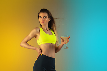 Image showing Fashion portrait of young fit and sportive woman drinking cocktail on gradient background. Perfect body ready for summertime.