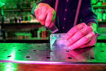 Image showing Close up of barman crushing a big piece of ice on the bar counter with a special bar equipment on it for a cocktail