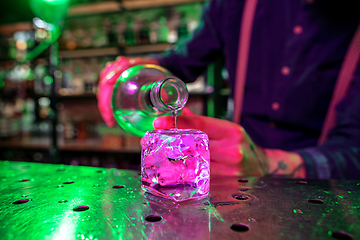 Image showing Close up of barman finishes preparation of alcoholic cocktail, pouring drink in multicolored neon light, focus on glass