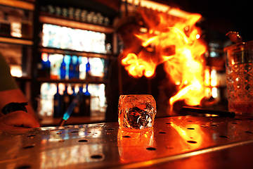 Image showing Close up big melting piece of ice on the bar counter in fireflames on it, preparation for a cocktail