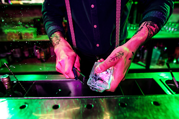 Image showing Close up of barman crushing a big piece of ice on the bar counter with a special bar equipment on it for a cocktail