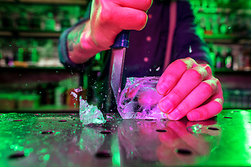 Image showing Close up of barman crushing a big piece of ice on the bar counter with a special bar equipment on it for a cocktail