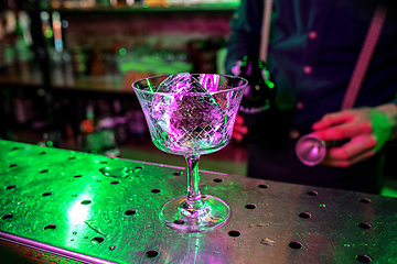 Image showing Close up of barman finishes preparation of alcoholic cocktail, pouring drink with shot in multicolored neon light, focus on glass