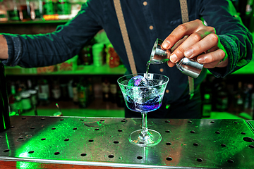 Image showing Close up of barman finishes preparation of alcoholic cocktail, pouring drink with shot in multicolored neon light, focus on glass