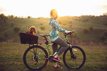 Image showing Young woman having fun near countryside park, riding bike, traveling with companion spaniel dog