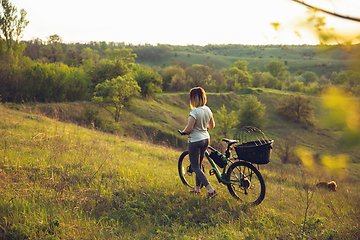 Image showing Young woman having fun near countryside park, riding bike, traveling with companion spaniel dog