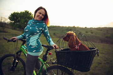 Image showing Young woman having fun near countryside park, riding bike, traveling with companion spaniel dog