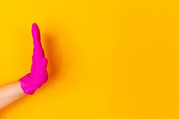 Image showing Hand in pink rubber glove greeting, waving isolated on yellow studio background with copyspace.