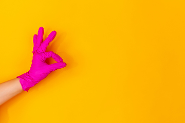 Image showing Hand in pink rubber glove showing nice sign isolated on yellow studio background with copyspace.