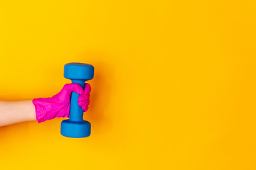 Image showing Hand in pink rubber glove holding dumbbell, gym weight isolated on yellow studio background with copyspace.
