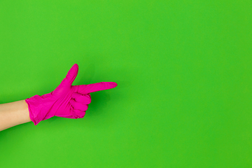 Image showing Hand in pink rubber glove pointing isolated on green studio background with copyspace.