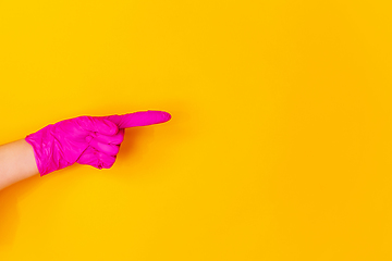 Image showing Hand in pink rubber glove pointing isolated on yellow studio background with copyspace.