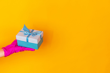 Image showing Hand in pink rubber glove holding gift isolated on yellow studio background with copyspace.