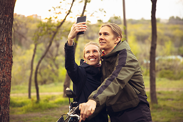 Image showing Best friends having fun near countryside park, resting after riding bikes, spending time together, sitting on the grass. Taking selfie.