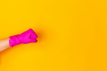 Image showing Hand in pink rubber glove showing fist bump isolated on yellow studio background with copyspace.