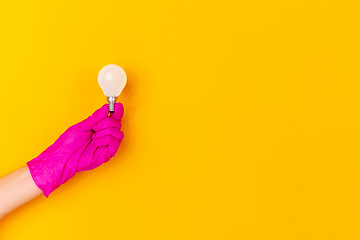 Image showing Hand in pink rubber glove holding lightbulb isolated on yellow studio background with copyspace.