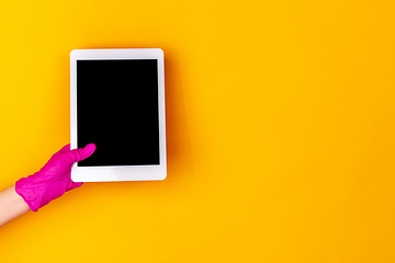 Image showing Hand in pink rubber glove holding tablet with blank screen isolated on yellow studio background with copyspace.