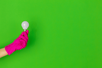 Image showing Hand in pink rubber glove with lightbulb isolated on green studio background with copyspace.