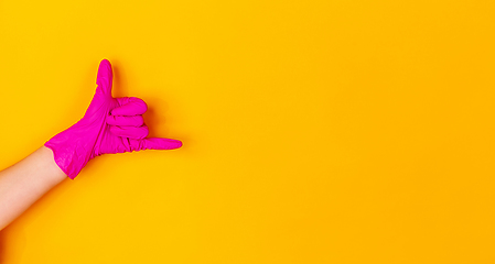 Image showing Hand in pink rubber glove isolated on yellow studio background with copyspace. Flyer.