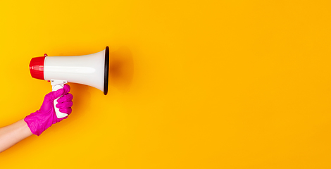 Image showing Hand in pink rubber glove holding megaphone isolated on yellow studio background with copyspace. Flyer.