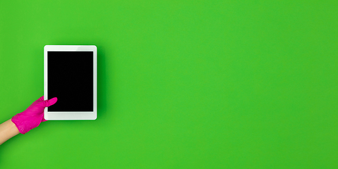 Image showing Hand in pink rubber glove holding tablet with blank screen isolated on green studio background with copyspace. Flyer.