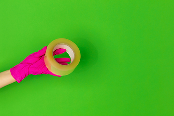 Image showing Hand in pink rubber glove with skotch tape isolated on green studio background with copyspace.