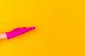 Image showing Hand in pink rubber glove taking, showing isolated on yellow studio background with copyspace.