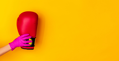 Image showing Hand in pink rubber glove holding boxer\'s glove isolated on yellow studio background with copyspace. Flyer.