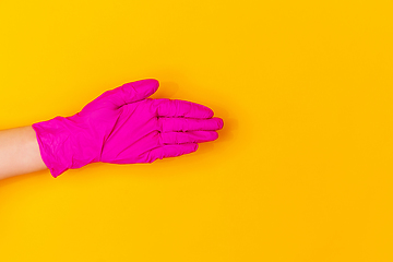 Image showing Hand in pink rubber glove greeting isolated on yellow studio background with copyspace.