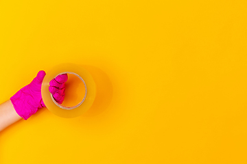 Image showing Hand in pink rubber glove holding skotch tape isolated on yellow studio background with copyspace.