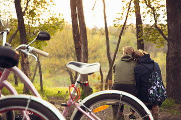 Image showing Best friends having fun near countryside park, resting after riding bikes, spending time together, sitting on the grass