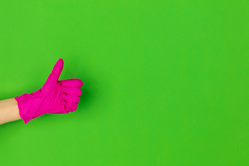 Image showing Hand in pink rubber glove showing thumb up isolated on green studio background with copyspace.