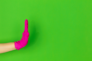 Image showing Hand in pink rubber glove clapping isolated on green studio background with copyspace.