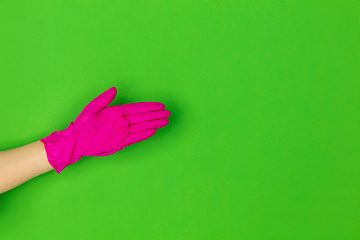 Image showing Hand in pink rubber glove greeting isolated on green studio background with copyspace.