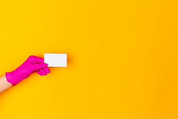 Image showing Hand in pink rubber glove holding business card isolated on yellow studio background with copyspace.