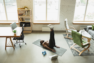 Image showing Young african-american man training at home during quarantine of coronavirus outbreak, doinc exercises of fitness, aerobic. Staying sportive suring insulation.