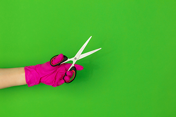 Image showing Hand in pink rubber glove holding sccissors isolated on green studio background with copyspace.