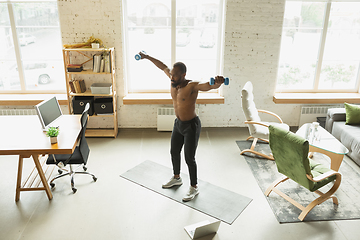 Image showing Young african-american man training at home during quarantine of coronavirus outbreak, doinc exercises of fitness, aerobic. Staying sportive suring insulation.