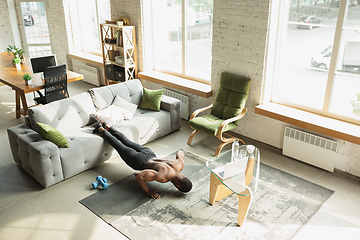 Image showing Young african-american man training at home during quarantine of coronavirus outbreak, doinc exercises of fitness, aerobic. Staying sportive suring insulation.