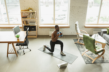 Image showing Young african-american man training at home during quarantine of coronavirus outbreak, doinc exercises of fitness, aerobic. Staying sportive suring insulation.