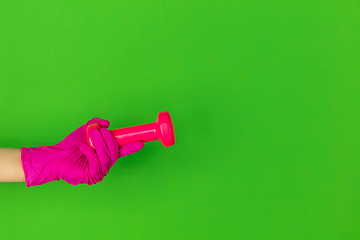 Image showing Hand in pink rubber glove holding gym weight, dumbbell isolated on green studio background with copyspace.