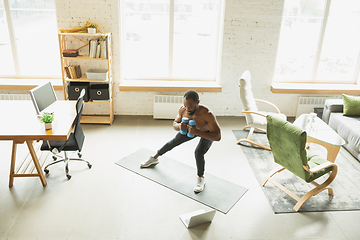 Image showing Young african-american man training at home during quarantine of coronavirus outbreak, doinc exercises of fitness, aerobic. Staying sportive suring insulation.