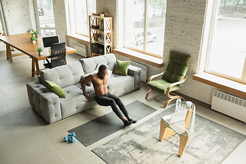 Image showing Young african-american man training at home during quarantine of coronavirus outbreak, doinc exercises of fitness, aerobic. Staying sportive suring insulation.