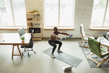 Image showing Young african-american man training at home during quarantine of coronavirus outbreak, doinc exercises of fitness, aerobic. Staying sportive suring insulation.