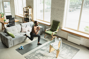 Image showing Young african-american man training at home during quarantine of coronavirus outbreak, doinc exercises of fitness, aerobic. Staying sportive suring insulation.