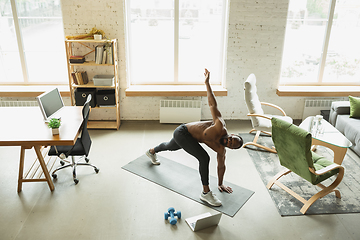 Image showing Young african-american man training at home during quarantine of coronavirus outbreak, doinc exercises of fitness, aerobic. Staying sportive suring insulation.