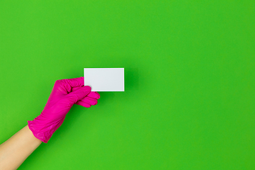 Image showing Hand in pink rubber glove holding business card isolated on green studio background with copyspace.