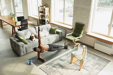 Image showing Young african-american man training at home during quarantine of coronavirus outbreak, doinc exercises of fitness, aerobic. Staying sportive suring insulation.