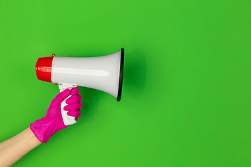 Image showing Hand in pink rubber glove holding megaphone isolated on green studio background with copyspace.