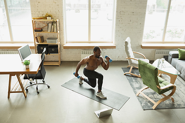 Image showing Young african-american man training at home during quarantine of coronavirus outbreak, doinc exercises of fitness, aerobic. Staying sportive suring insulation.